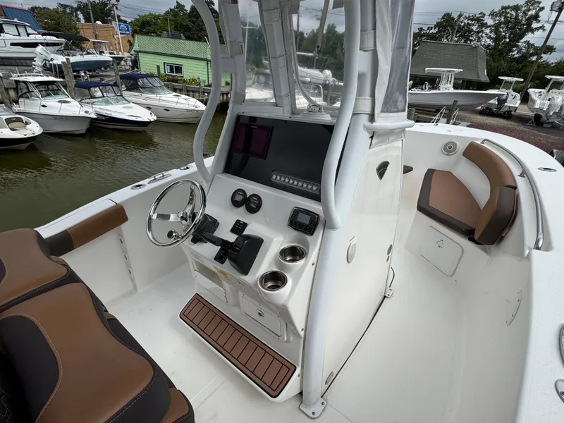 Slide: The Image of 2017 Tidewater 230 CC Adventure boat interior with helm, seating, and docked boats in background. - 12