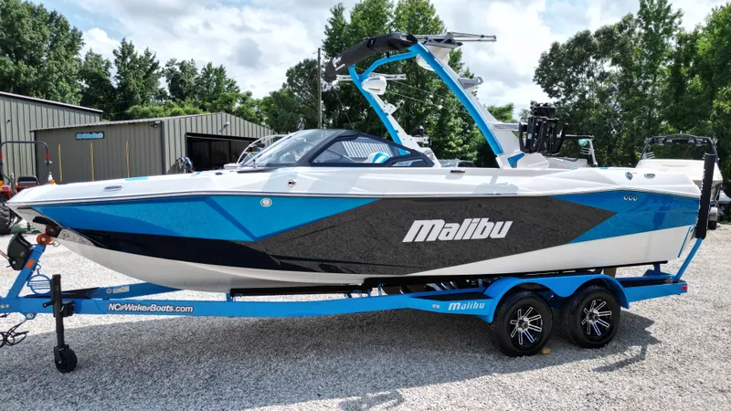 Slide: The Image of 2025 Malibu Wakesetter 23 LSV boat on trailer, blue and white design, parked outdoors. - 16