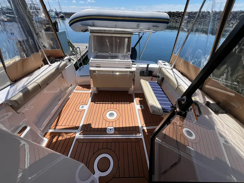 Slide: The Image of 2020 Ranger Tugs R-27 boat interior with teak flooring and seating, docked by calm water. - 13