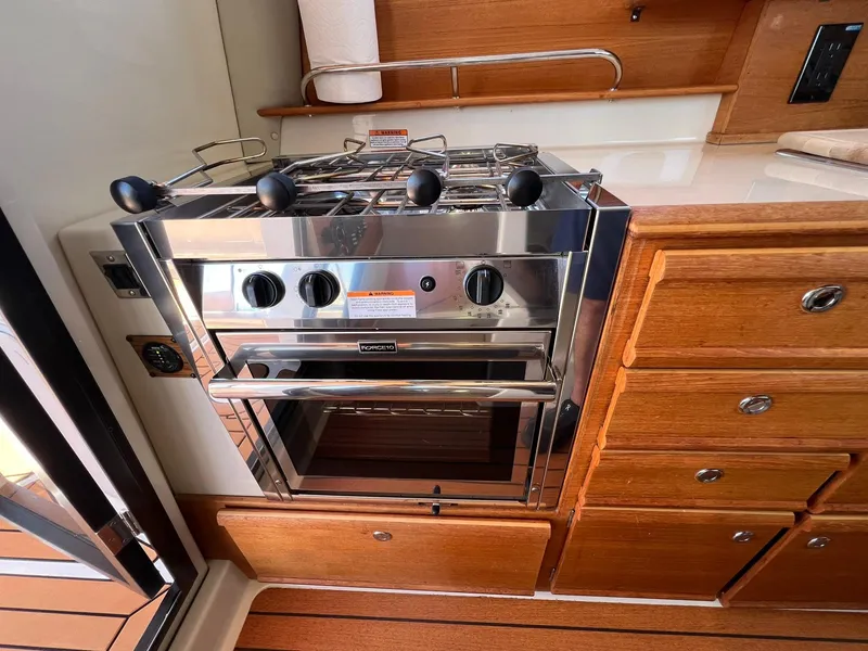Slide: The Image of 2020 Ranger Tugs R-27 galley with stainless steel stove and wooden cabinetry. - 17
