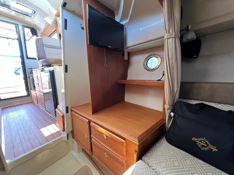 Slide: The Image of 2020 Ranger Tugs R-27 interior with TV, wooden cabinetry, and porthole window. - 26