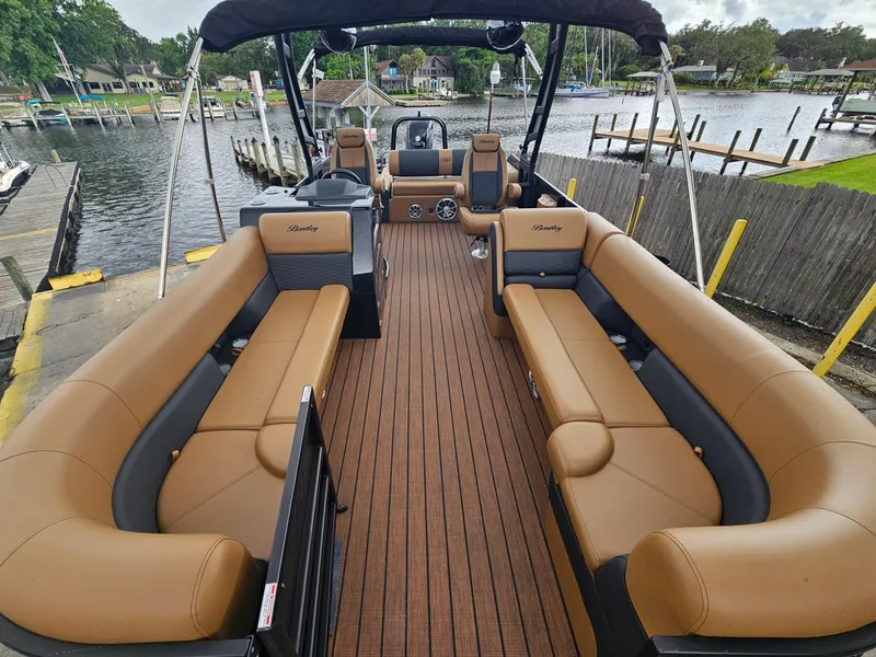 Slide: The Image of 2026 Bentley Pontoons Elite 253 Swingback with luxurious seating, docked by a scenic waterfront. - 13