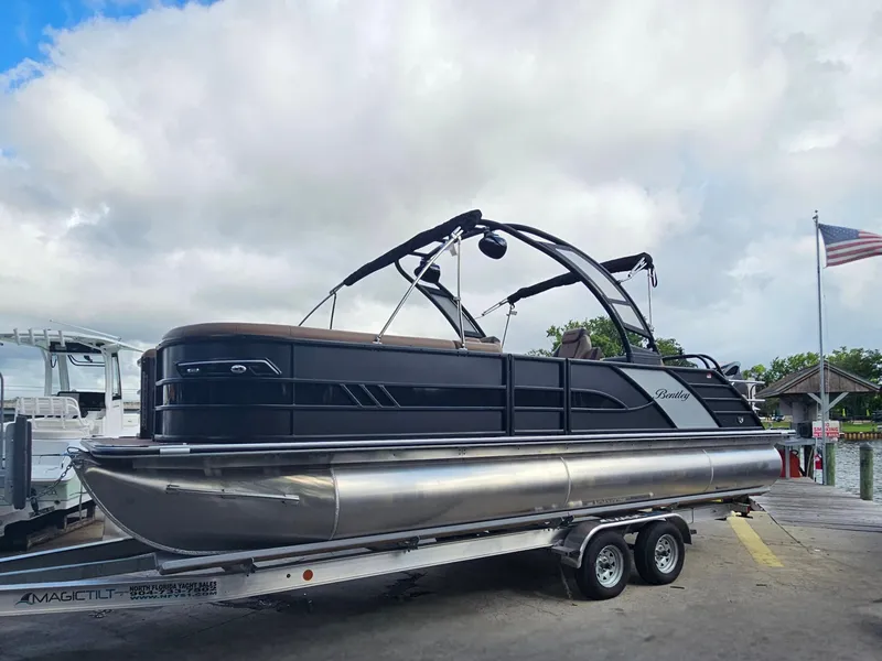Slide: The Image of 2026 Bentley Pontoons Elite 253 Swingback on trailer at marina, under cloudy sky. - 34