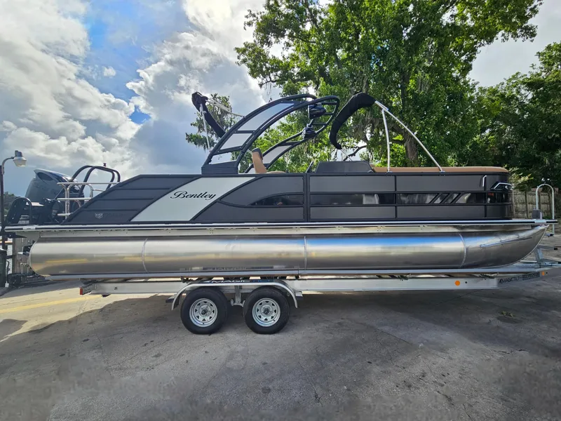 Slide: The Image of 2026 Bentley Pontoons Elite 253 Swingback on trailer, sleek design, parked outdoors. - 5