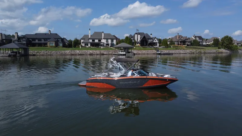 Slide: The Image of 2016 MasterCraft X23 boat on a calm lake with waterfront homes in the background. - 0