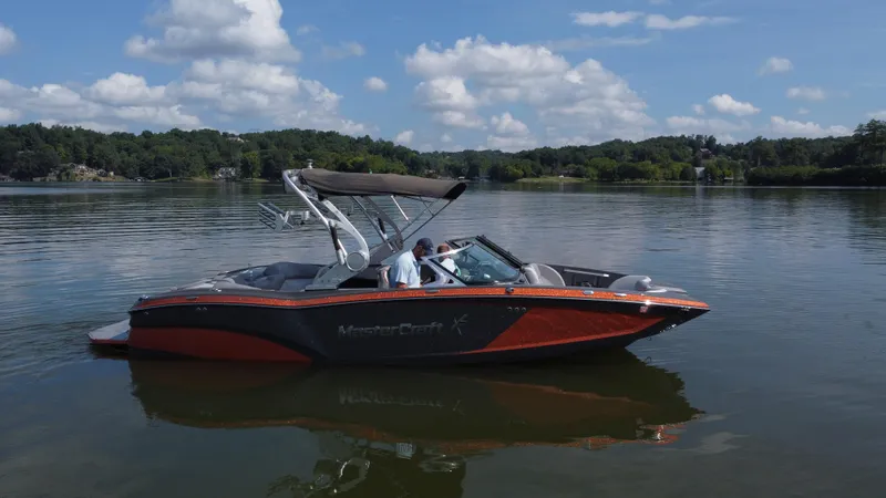 Slide: The Image of 2016 MasterCraft X23 boat on a calm lake under a blue sky. - 1