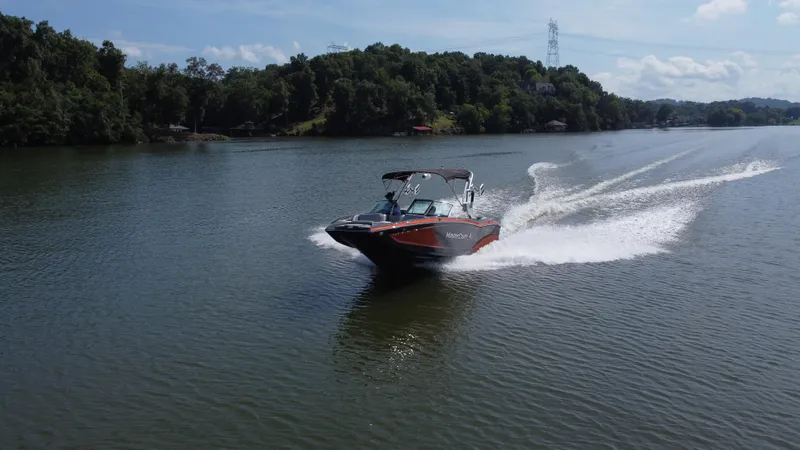 Slide: The Image of 2016 MasterCraft X23 speedboat cruising on a scenic lake with lush green surroundings. - 10