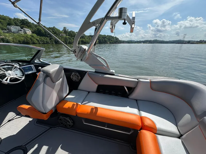Slide: The Image of 2016 MasterCraft X23 boat interior with orange and gray seating on a sunny lake. - 13