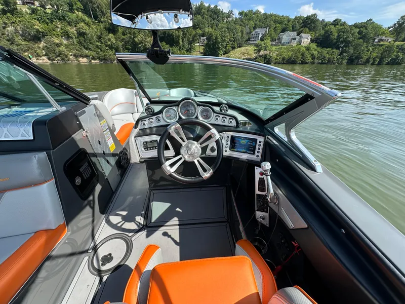Slide: The Image of 2016 MasterCraft X23 boat interior with modern dashboard and orange seating on a lake. - 14