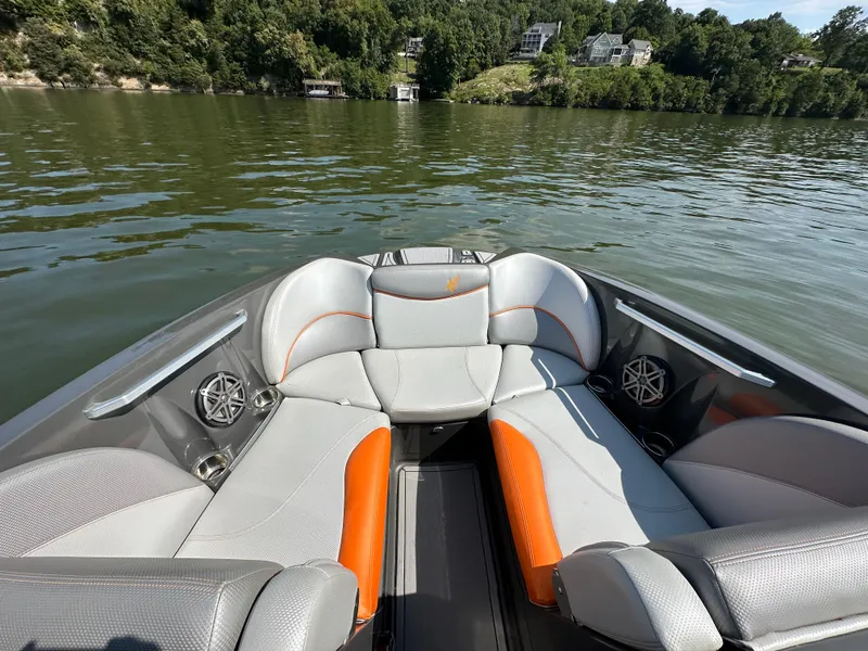Slide: The Image of 2016 MasterCraft X23 boat interior with gray and orange seating on a calm lake. - 15
