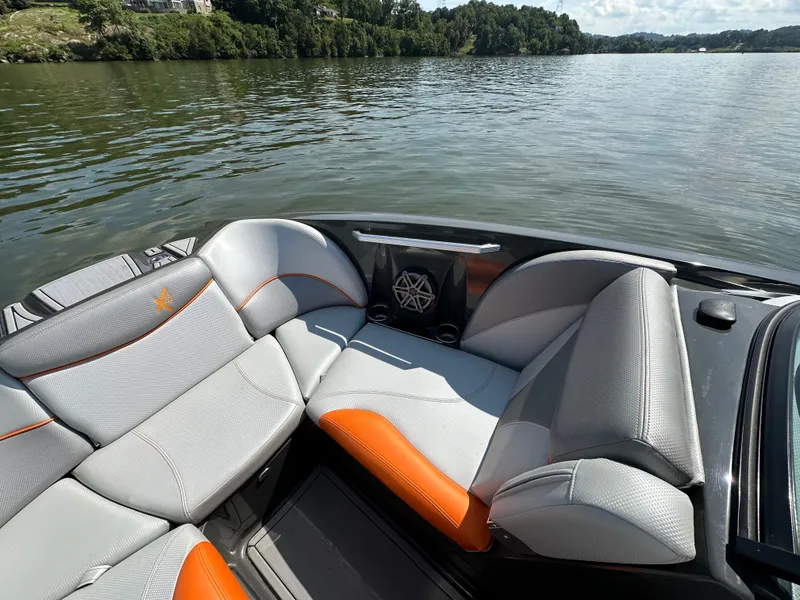 Slide: The Image of 2016 MasterCraft X23 boat interior with gray and orange seating on a calm lake. - 16