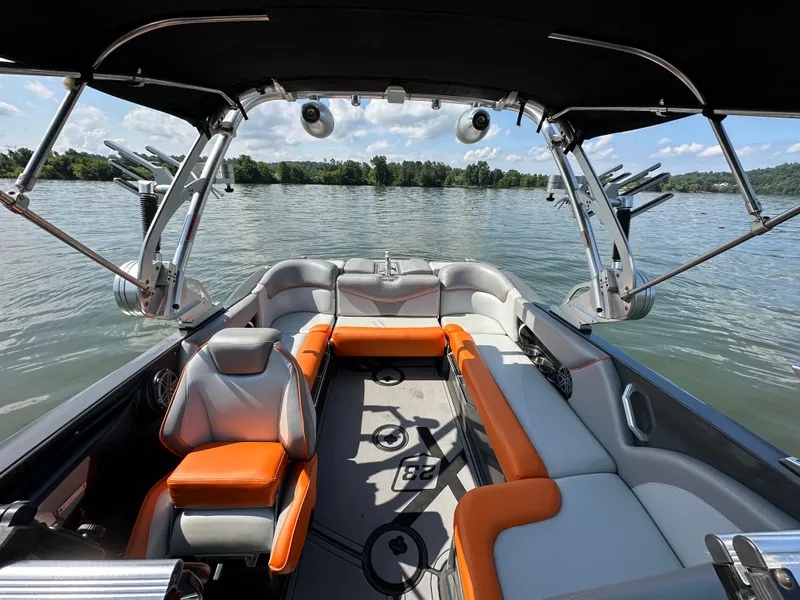 Slide: The Image of 2016 MasterCraft X23 boat interior with orange and gray seating on a calm lake. - 18