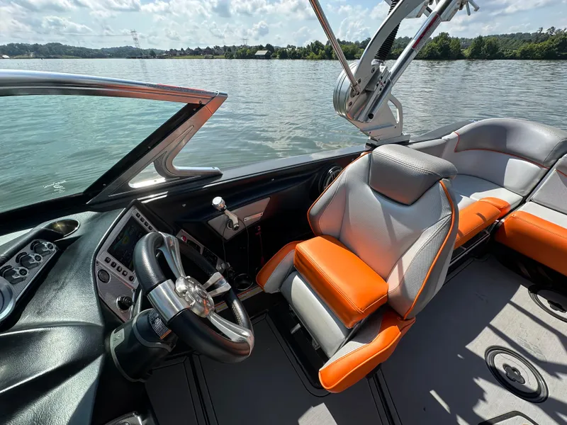 Slide: The Image of 2016 MasterCraft X23 boat interior with orange and gray seating, steering wheel, and lake view. - 22