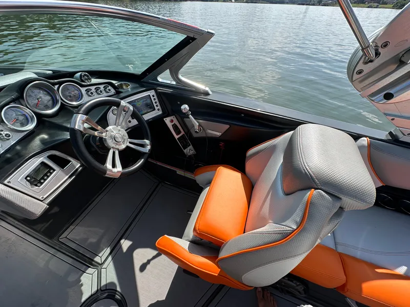Slide: The Image of 2016 MasterCraft X23 boat interior with orange and gray seating, steering wheel, and dashboard controls. - 23