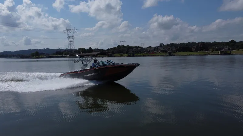 Slide: The Image of 2016 MasterCraft X23 speedboat cruising on a calm lake under a partly cloudy sky. - 9