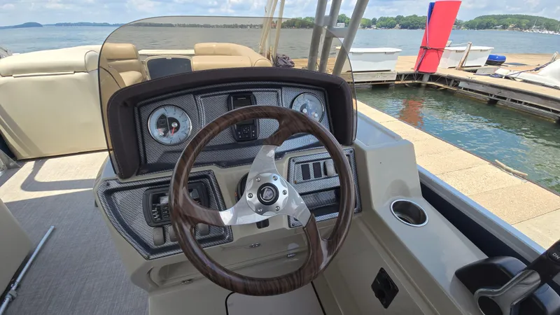 Slide: The Image of 2017 Premier 240 SunSation boat dashboard with steering wheel, docked by a scenic lake. - 20