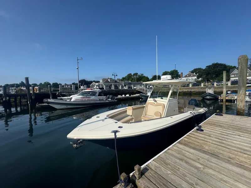 Slide: The Image of 2023 Scout 255 LXF boat docked at a marina under clear blue skies. - 24