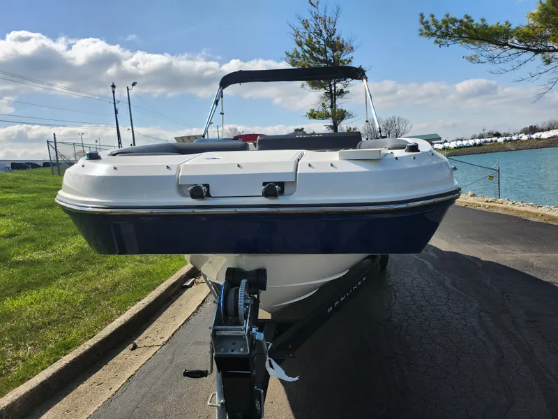 Slide: The Image of 2021 Bayliner DX 2000 boat on trailer, parked near water under a clear sky. - 6