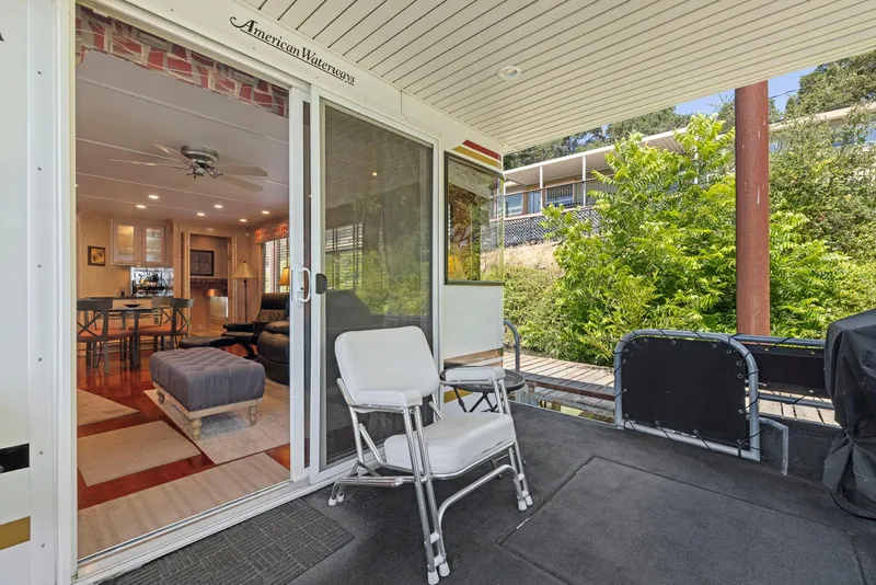 Slide: The Image of 2007 American Waterways Widebody houseboat interior with open sliding doors, chairs, and lush greenery outside. - 21