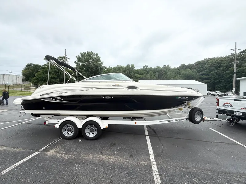 The Image of 2006 Sea Ray 240 Sundeck boat on trailer in parking lot, overcast sky. - 1