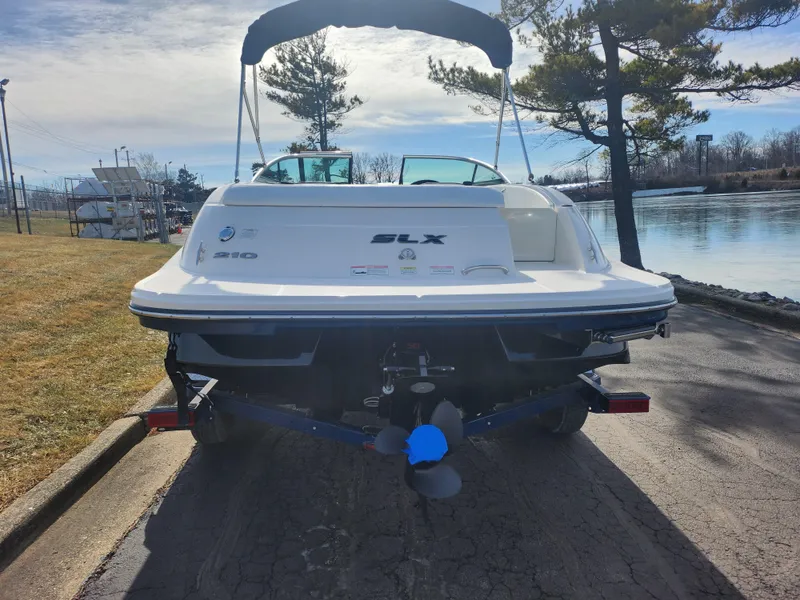 Slide: The Image of 2014 Sea Ray 210 SLX boat on trailer by a lakeside, under a clear sky. - 2