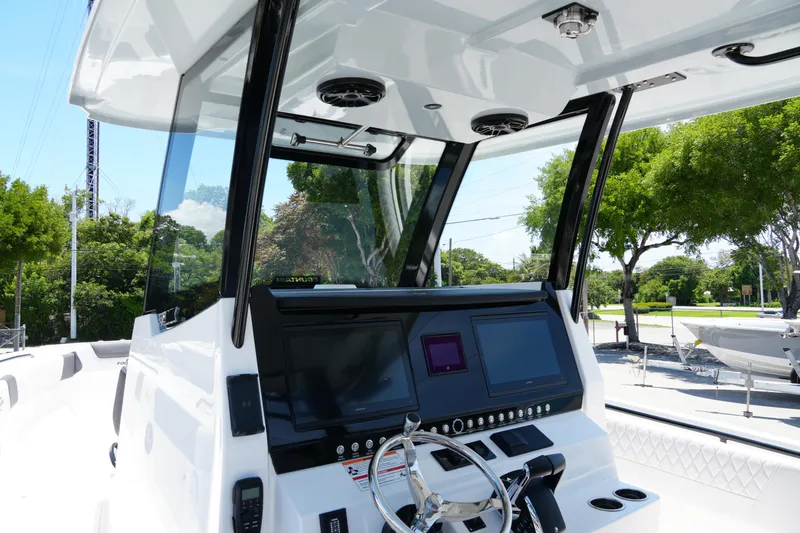 Slide: The Image of 2025 Fountain 32NX boat dashboard with modern controls and steering wheel, surrounded by lush greenery. - 18