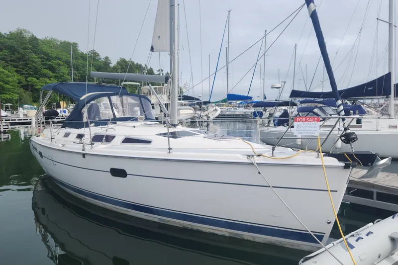 The Image of 2004 Hunter 36 sailboat docked, for sale, with blue canopy and lush green background. - 0