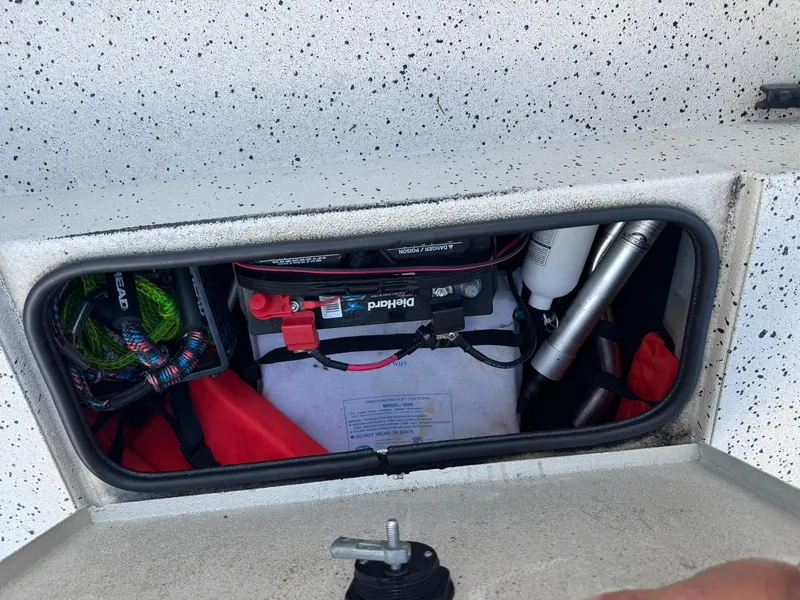 Slide: The Image of Open storage compartment in 2016 Xpress HD16DB boat, showing battery and equipment. - 8