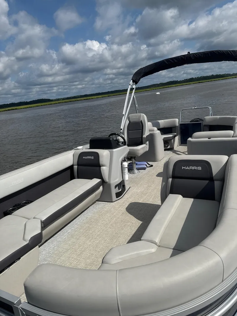 Slide: The Image of 2024 Harris Cruiser 230 pontoon boat on a lake under a cloudy sky. - 1