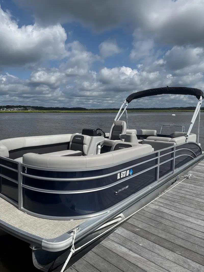 Slide: The Image of 2024 Harris Cruiser 230 pontoon boat docked on a sunny day with cloudy sky. - 2