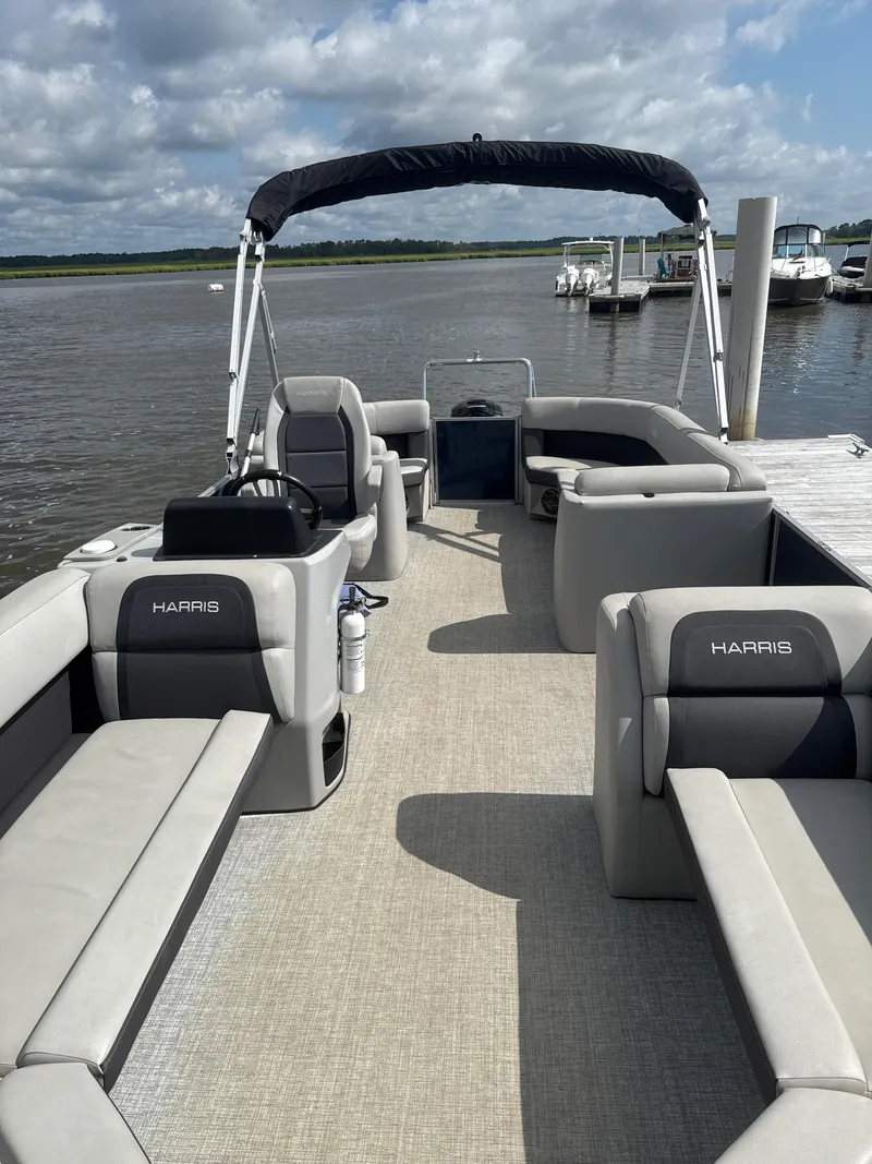 Slide: The Image of 2024 Harris Cruiser 230 pontoon boat with spacious seating, docked by a calm lake. - 3