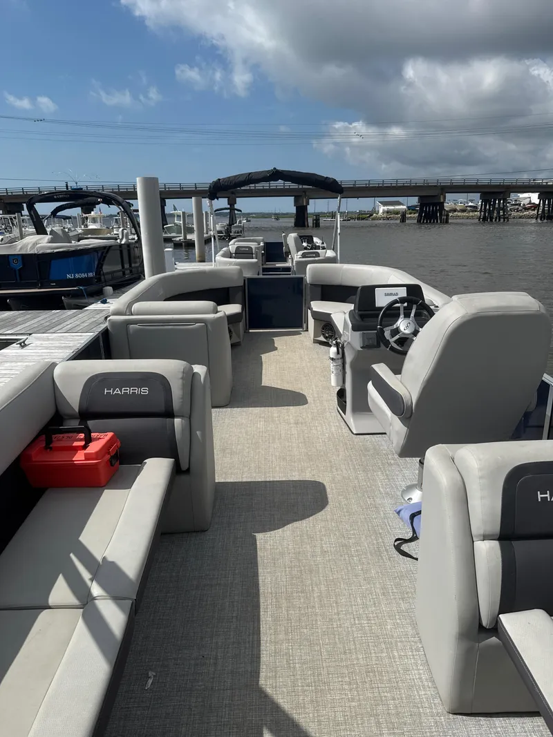 Slide: The Image of 2024 Harris Cruiser 230 pontoon boat interior with gray seating, docked by a bridge. - 7