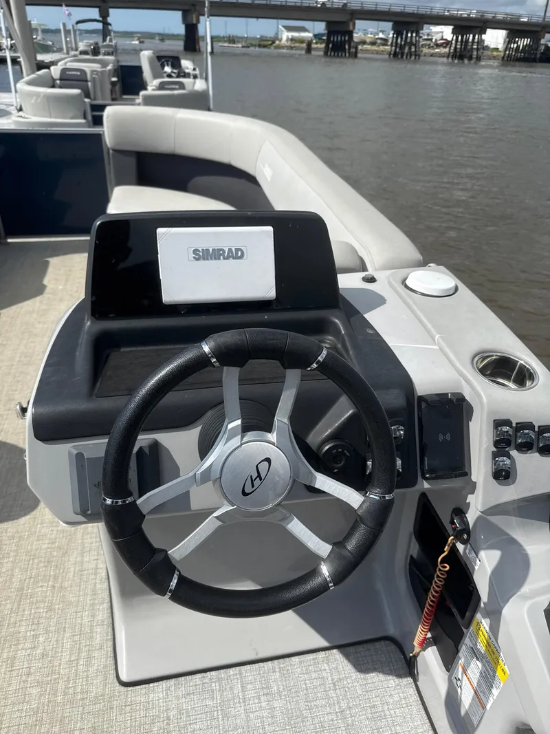 Slide: The Image of 2024 Harris Cruiser 230 boat dashboard with steering wheel and Simrad display, near a bridge. - 8
