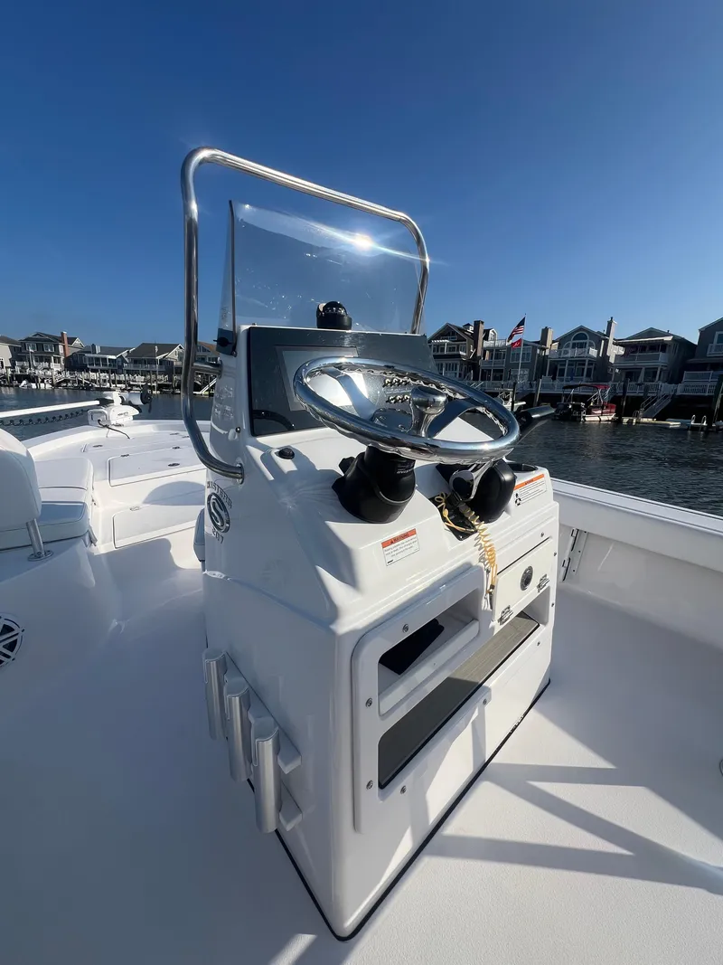Slide: The Image of 2023 Sportsman Masters 207 Bay Boat console with steering wheel, docked near waterfront homes. - 10