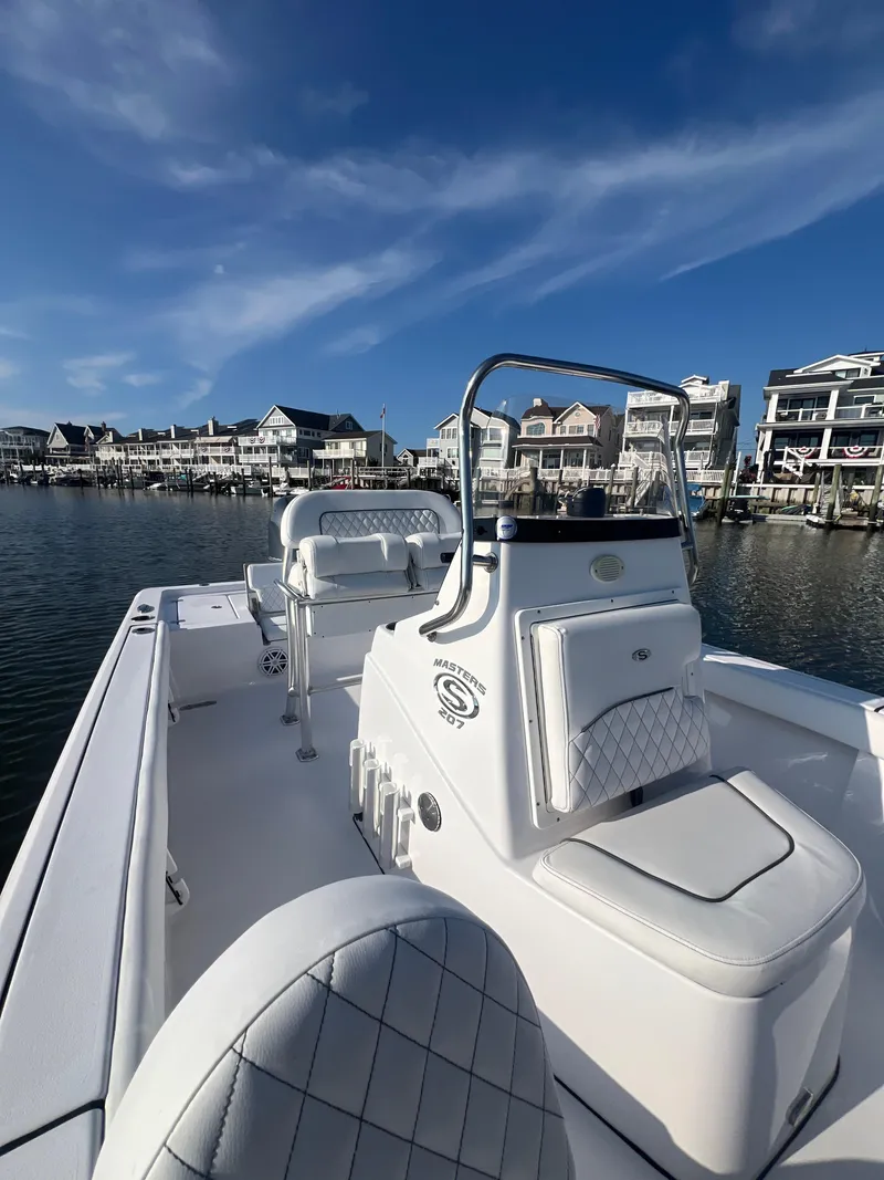 Slide: The Image of 2023 Sportsman Masters 207 Bay Boat docked near waterfront homes under clear blue sky. - 8