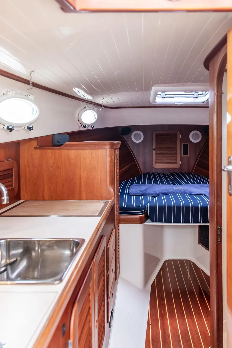 Slide: The Image of 1999 Hinckley Picnic Boat Classic interior with wood finish, kitchenette, and cozy sleeping area. - 18