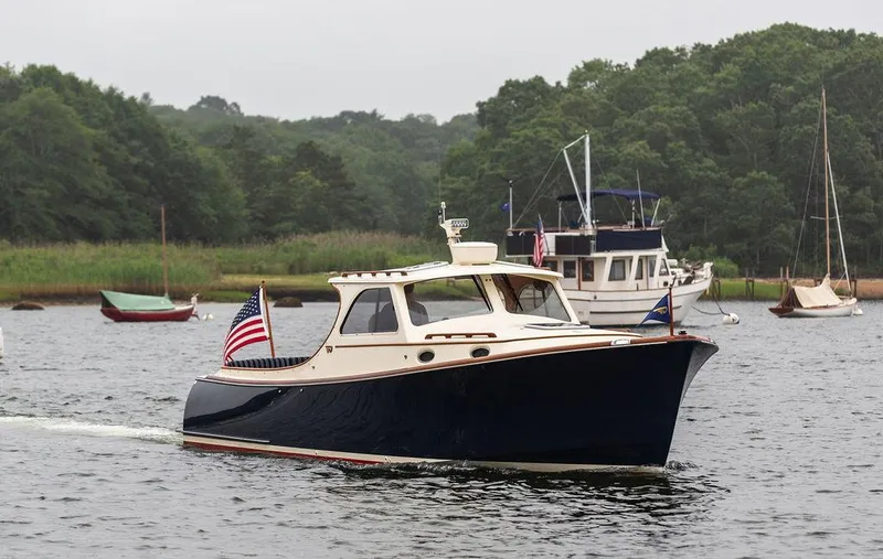 Slide: The Image of 1999 Hinckley Picnic Boat Classic cruising on a serene lake with lush green surroundings. - 5