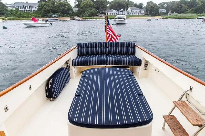 Slide: The Image of 1999 Hinckley Picnic Boat Classic with striped seating, American flag, and scenic waterfront view. - 9