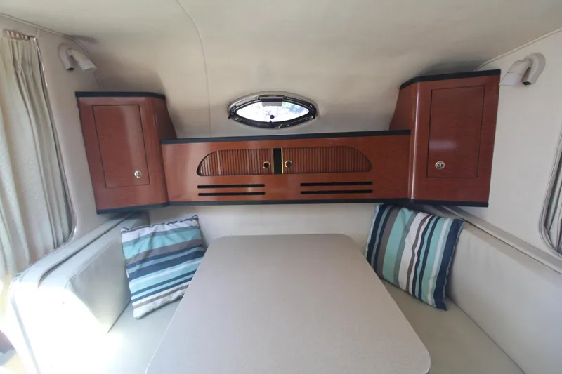 Slide: The Image of 2004 Sea Ray 280 Sundancer cabin interior with table, striped cushions, and wooden cabinets. - 16