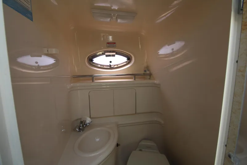 Slide: The Image of 2004 Sea Ray 280 Sundancer bathroom interior with sink, toilet, and porthole window. - 21