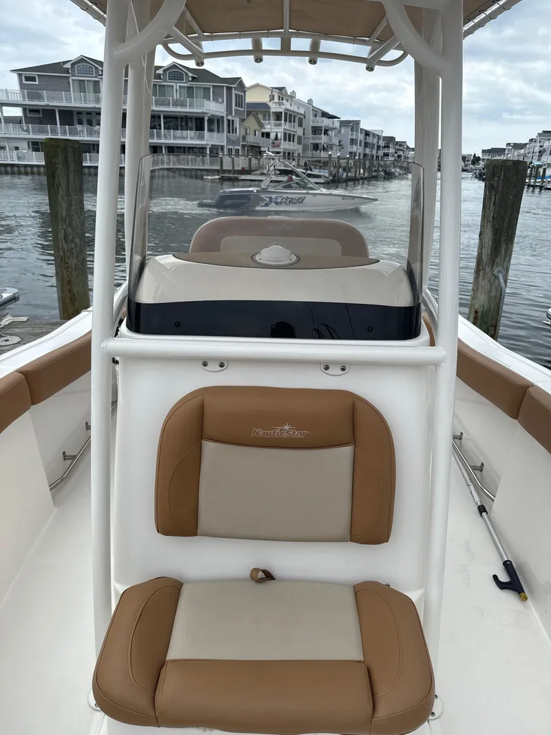 Slide: The Image of 2023 NauticStar 22L boat interior with tan seating, docked near waterfront homes. - 4