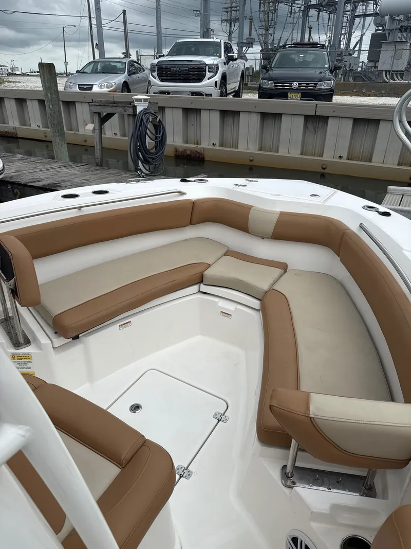 Slide: The Image of 2023 NauticStar 22L boat with tan and cream seating, docked near parked cars. - 6