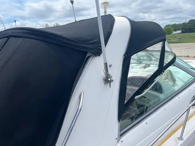 Slide: The Image of 1998 Sea Ray 290 Sundancer boat with black canopy and windshield, docked under cloudy sky. - 4