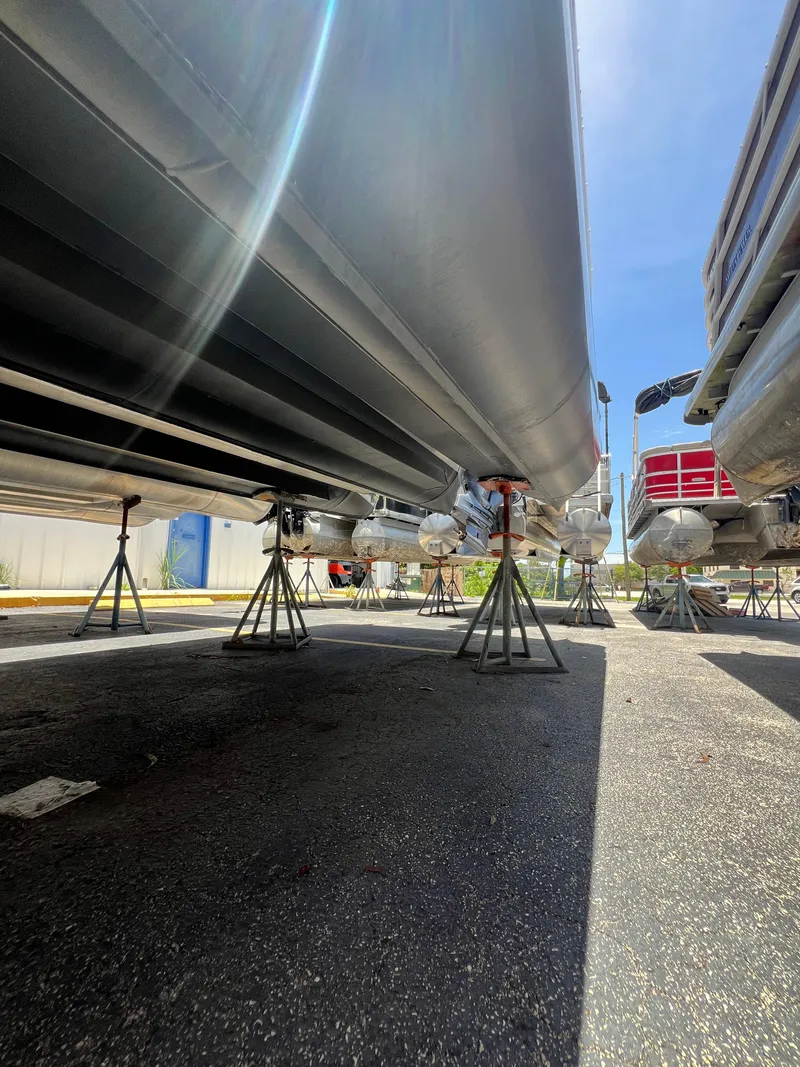 Slide: The Image of 2022 Godfrey Monaco 235 SDB pontoon boats on stands, viewed from below, sunny day. - 22