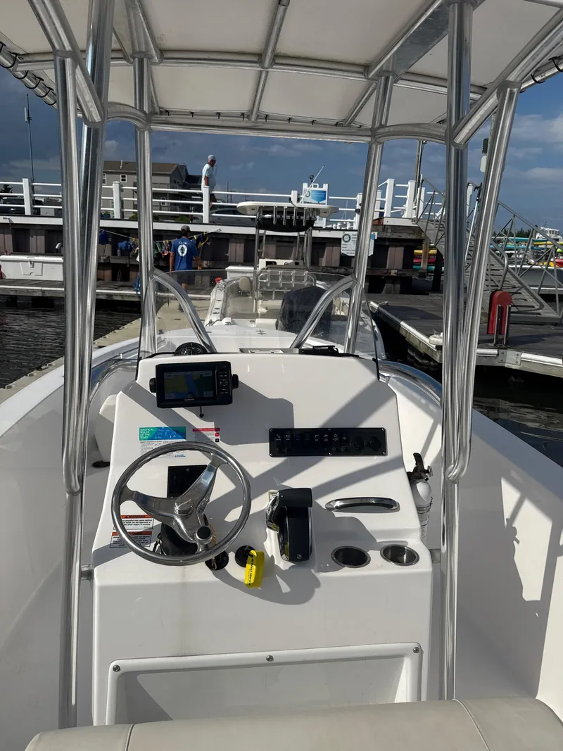 Slide: The Image of 2024 Aquasport 2200 Center Console boat interior at marina, featuring steering and control panel. - 2