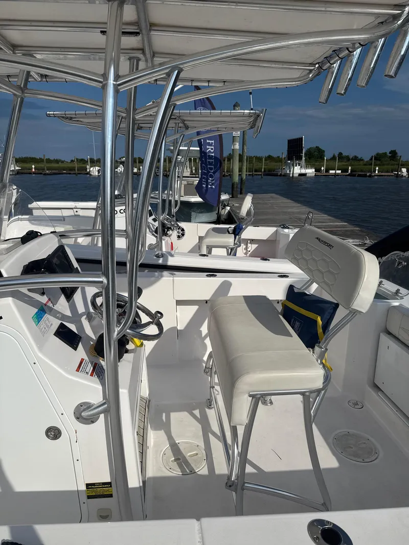 Slide: The Image of 2024 Aquasport 2200 Center Console boat interior with seating and controls, docked by the water. - 7