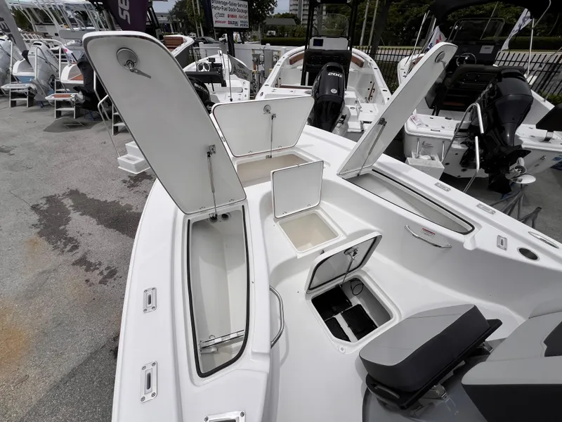 Slide: The Image of 2026 Sea Pro 230 DLX boat with open storage compartments and seating, displayed at a marina. - 27