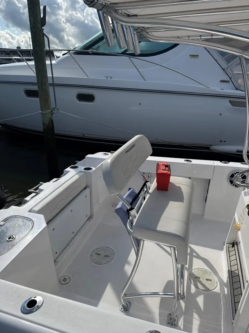 Slide: The Image of 2023 Aquasport 2200 Center Console boat interior with seating and storage, docked beside another vessel. - 2