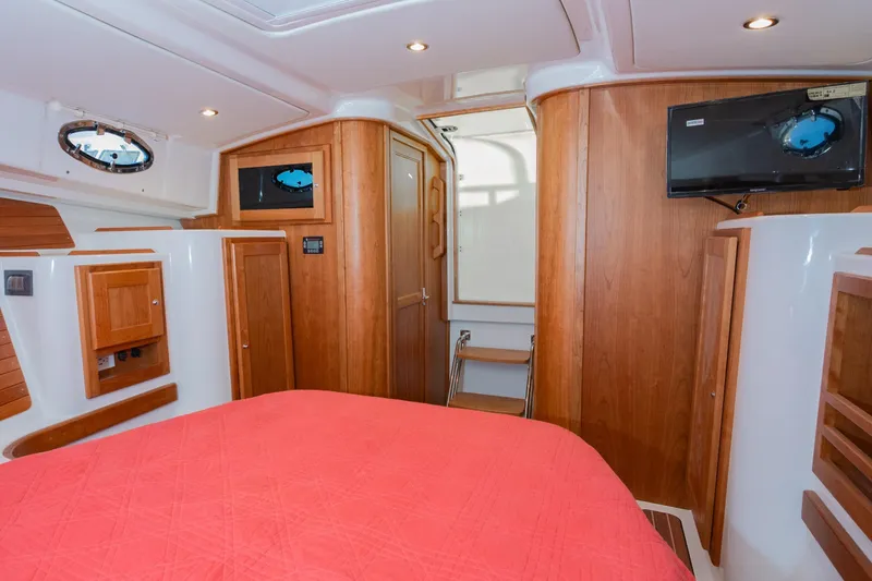 Slide: The Image of 2026 Back Cove 34O cabin interior with wood paneling, red bedding, and mounted TV. - 13