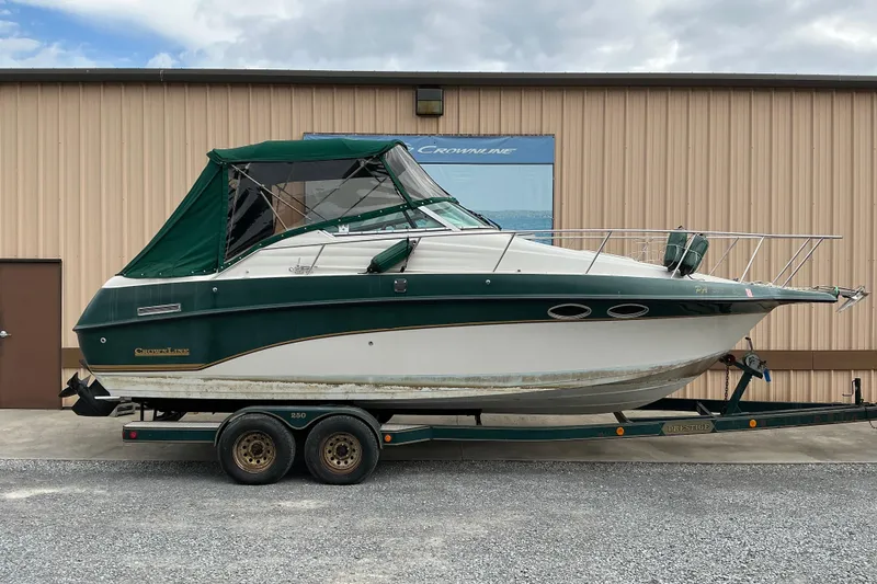 The Image of 1996 Crownline 250 CR boat with green canopy on trailer, parked outside a building. - 0